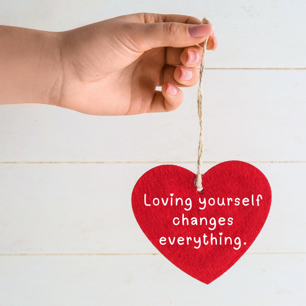 Woman's hand holding a fabric heart that says "Loving yourself changes everything"