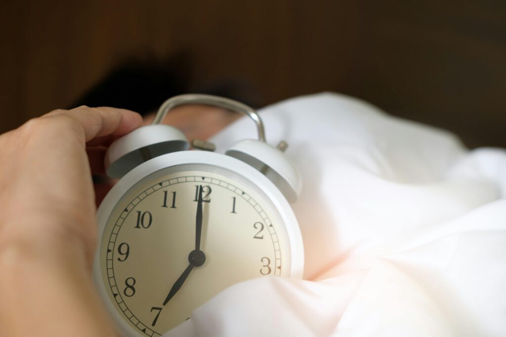 person in bed holding an alarm clock 
